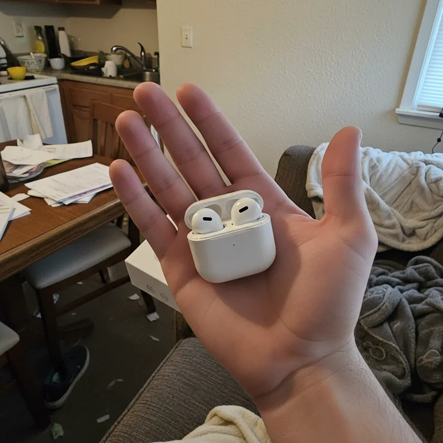 Fone de ouvido bluetooth branco com estojo, segurado na mão dentro de casa com luz fraca